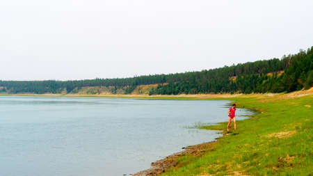 Yakut Asian girl the lady angler goes fishing spinning reel in a bathing suit along the wild North of the Vilyui river to the forest.の写真素材