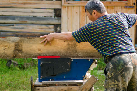 Adult Yakut man saws a Board on a saw against a house of timber in the Yakut village.の写真素材