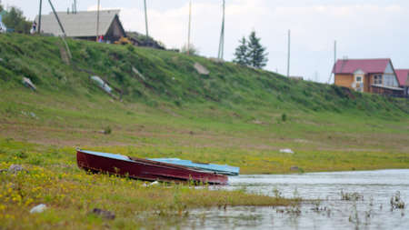 Old metal boat stands on land in the grass on the shore of the village houses of Northern Yakutia Suntar.の写真素材