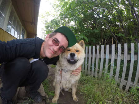 Russian man with glasses takes a selfie with a dog breed Akita inu on the private territory of a residential building in Yakutia.の写真素材