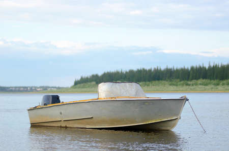 Old metal boat is in calm water with reflection of clouds, was chained against the background of the Yakut of the Northern villages in the forest Suntar.の写真素材