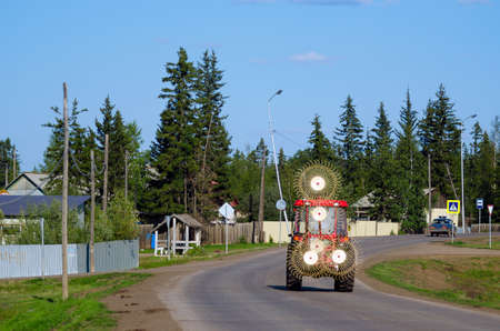 Tractor with a device for collecting hay rides on the road among the houses of the Northern village of Suntar in Yakutia.の写真素材
