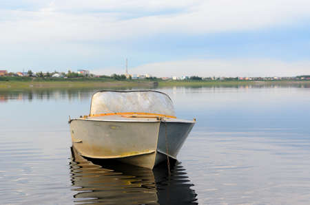 Metal old the boat is in calm water with reflection of clouds chained in the background of the Yakut of Northern villages in the forest Suntar.の写真素材