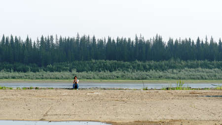 The girl-traveler on the edge of an abandoned stone pier sits resting and taking photos on the phone in the North of Yakutia near the vilyu river.の写真素材
