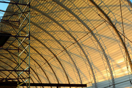 The construction of the roof of the new hangar in a semi-circle of metal with the shadows of the structure at sunset.の写真素材