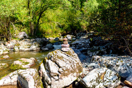 A pyramid of flat round stones stands on a large stone in the middle of a mountain rapid river in the Altai during the day in the forest.の写真素材