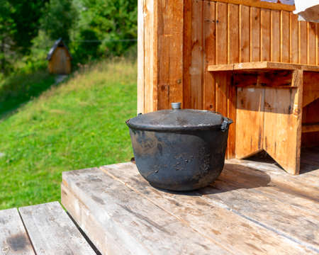 A large, black from soot, the cauldron, the pot stands on the edge of a wooden house a bright day amid toilet and herbs.の写真素材