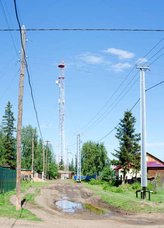 Power lines on concrete poles protected from impact by a car from below stand on a village street next to a puddle in the Northern Yakut village of Suntar.の写真素材