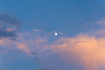 Incomplete moon in the sky during sunset at dusk.の写真素材