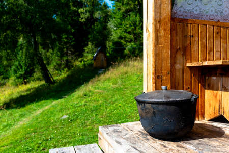 A large, black from soot, the cauldron, the pot stands on the edge of a wooden house a bright day amid toilet in the woods and grass on the field.の写真素材