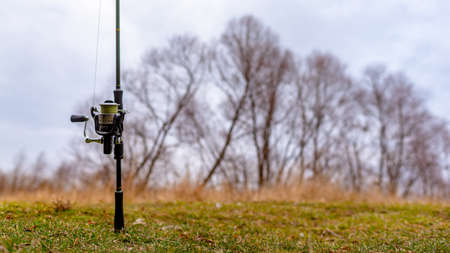 Fishing rod spinning reel stands on the background of the field and trees in autumn.の写真素材