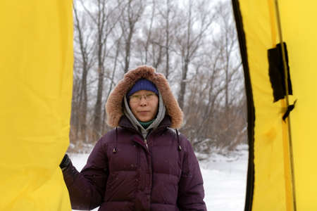Asian girl angler with the glasses and the hood looking at the tent opening the door from the street coming from snow and Blizzard.の写真素材