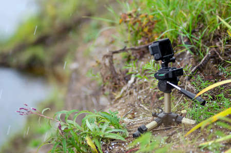 Action camera on a small tripod stands in the grass of the river under the flying snow flakes.の写真素材