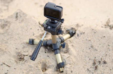 Action camera stands on a small tripod, recording video on a sandy beach.の写真素材