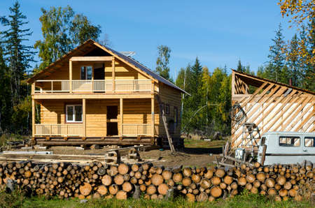 A new private cottage of yellow pine logs stands among spruce forests and wild forest firewood in the taiga of Yakutia, next to the remains of an iron garbage truck in the village of ulus Suntar.のeditorial素材