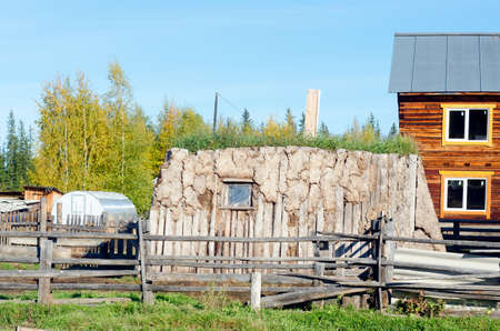The room for cattle hoton, made of cow dung and wood, overgrown with grass stands on a modern plot with a house in the North of Yakutia.のeditorial素材
