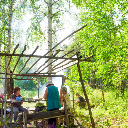 Lunch in the forest of the North of Yakutia. Women at a wooden table communicate and cook, and men at the fire in the smoke cook soup.の写真素材