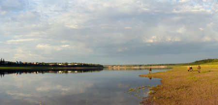Two elderly men and two Yakut women talking walk along the Bank of the Northern Viluy river at sunset against the background of the houses of the village of Suntar on the other Bank.の写真素材