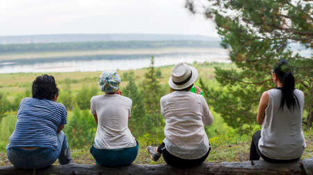 Four girls Yakut friends of tourists sitting resting backs on a log on the mountain overlooking the North river vilyu and taiga.の写真素材