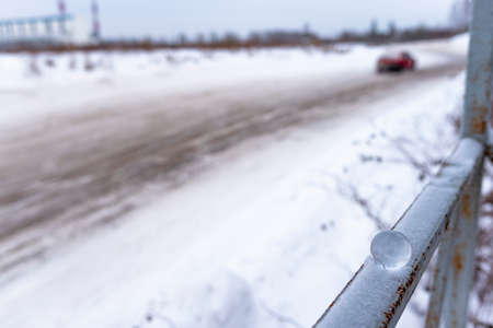 A small glass ball lies in winter on the railing in the snow on the background of a dirty road with a car leaving.の写真素材