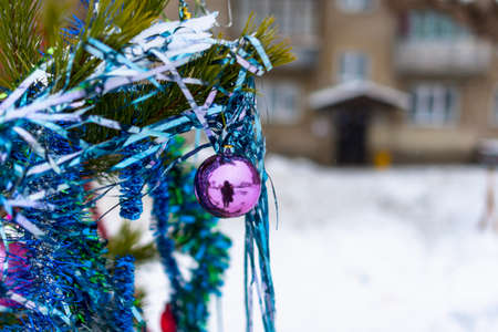 Christmas tree stands decorated with balloons, garlands and tinsel in a snowdrift on the street in the Russian city in the courtyard of a large apartment building on the background of the entrance and Windows.の写真素材