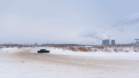 Russia, Novosibirsk - November 30, 2019. Russian low dark car "VAZ Zhiguli" goes quickly turning the wheel in front of the pipes of the thermal power plant in the winter in the snow.のeditorial素材