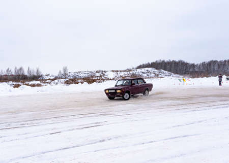 Russia, Novosibirsk - November 30, 2019. Russia, Novosibirsk-November 30, 2020. Russian dark car "VAZ-Zhiguli" goes fast sideways in a drift and on a turn in the snow with a young driver-a man and a woman-passenger in the winter.のeditorial素材