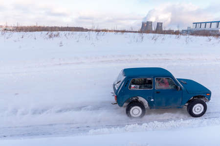 Russia, Novosibirsk-January 20, 2020 Russian SUV "Lada Niva" is driving fast on a snowy road in a field in winter against the background of pipes with smoke.のeditorial素材
