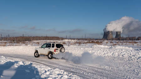 Russia, Novosibirsk-January 20, 2020 Four-wheel drive 4x4 white SUV "Suzuki Escudo" quickly goes on a snowy road in winter with clouds of smoke against the background of the pipes of the heat power station.のeditorial素材