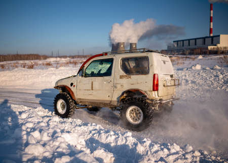 Russia, Novosibirsk-January 20, 2020 4x4 four-wheel-drive SUV "Suzuki Jimny" goes quickly raising snow in winter on the road against the background of smoke from the pipes of the CHP.のeditorial素材