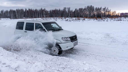 Russia, Novosibirsk-January 20, 2020 Russian white SUV "UAZ Patriot" quickly goes on a snowy road in the field in winter against the background of the forest clinging to the snowstorm wheel.のeditorial素材