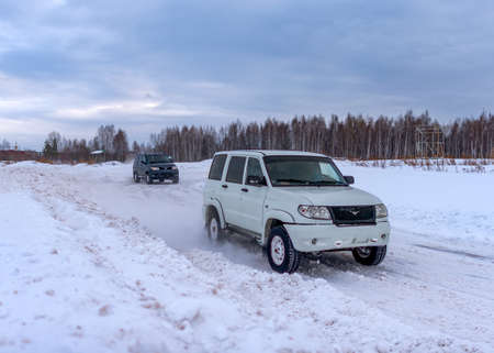 Russia, Novosibirsk-January 20, 2020 Two Russian UAZ Patriot off-road vehicles, white and dark, are driving fast on a snowy road in a field in winter, clinging to a snowstorm with a wheel.のeditorial素材