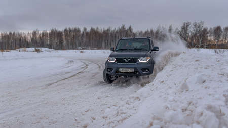 Russia, Novosibirsk-January 20, 2020 Russian SUV "UAZ Patriot" quickly goes on a snowy road in the field in winter, clinging to the bumper snowstorm wheel.のeditorial素材