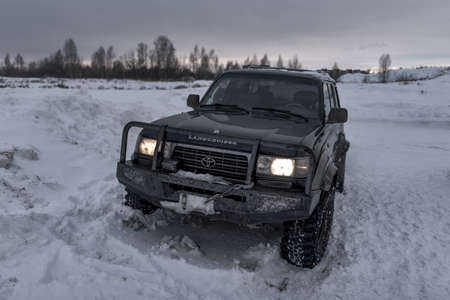Russia, Novosibirsk-January 20, 2020 4x4 all-wheel drive SUV "Toyota land cruiser" with an iron protective bumper stands in the winter in the snow in the semi-darkness with the headlights on.のeditorial素材