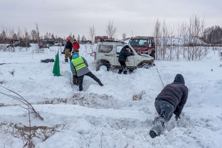 Russia, Novosibirsk-January 20, 2020 Stuck 4x4 four-Wheel drive SUV "Suzuki Jimny" pulls itself out using a winch cable and an anchor with an assistant in the snow.のeditorial素材