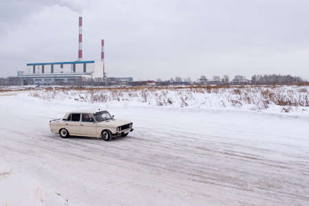 Russia, Novosibirsk - November 30, 2019. An old Russian car VAZ Zhiguli goes, turning the wheel, with a passenger on the road against the background of Smoking pipes of the heat power station.のeditorial素材