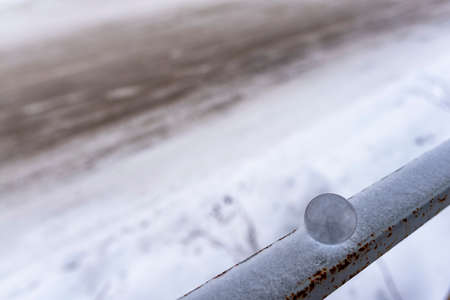 A small glass ball lies in winter on the railing in the snow against the background of a muddy road.の写真素材