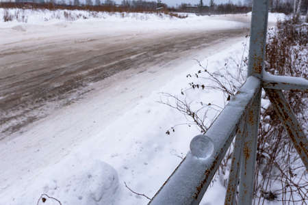A small glass ball lies in the winter on the railing in the snow against the background of a turn in the muddy road.の写真素材