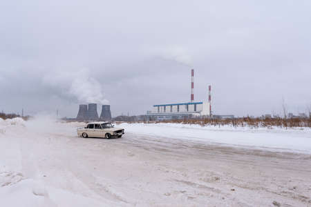 Russia, Novosibirsk - November 30, 2019. An old Russian white car VAZ Zhiguli is going fast in the drift, turning the wheel, on the road against the background of Smoking pipes of the heat power station.のeditorial素材