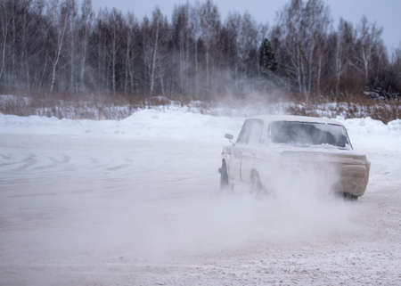Russia, Novosibirsk - November 30, 2019. Russian modified old car "VAZ-Zhiguli" goes fast drift turning the wheels raising snow with a camera "Gopro" on the roof on the turn.のeditorial素材