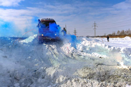 Russia, Novosibirsk - March 13, 2020. An off-road SUV "Range Rover 4x4" drives down a snowy mountain in colored blue smoke with a man outside.のeditorial素材