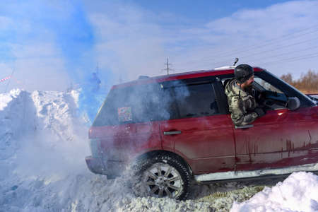 Russia, Novosibirsk-March 13, 2020. SUV "Range Rover" 4x4 quickly actively drives through the snow in blue smoke, and a man looking out of the window in a hard hat looks at the road.のeditorial素材