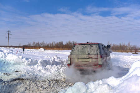 Russia, Novosibirsk - March 13, 2020. Offroad SUV "Range Rover 4x4" leaves on a bad snowy road in winter with a man leaning out of the window, raising a Blizzard.のeditorial素材