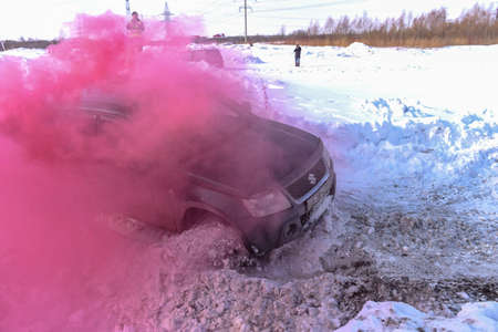 Russia, Novosibirsk-March 13, 2020. Offroad SUV "Suzuki Grand Vitara" 4x4 is rapidly actively driving on a broken road in clouds of colored crimson smoke with snow and mud from under the wheels.のeditorial素材