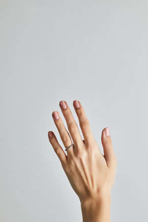 Womanâs hand with soft pink manicure and a delicate diamond band ring, posed against a neutral grey backgroundの写真素材