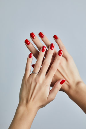 Womanâs hand with bold red manicure and a simple silver ring, posed against a neutral grey backgroundの写真素材