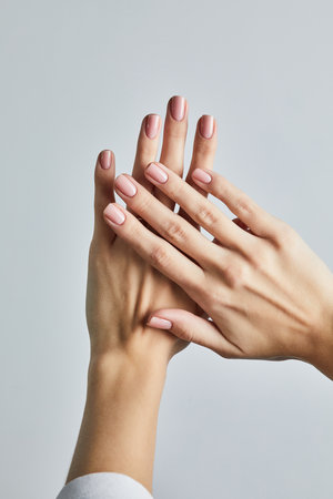 Womanâs hand with soft pink manicure, posed against a neutral grey backgroundの写真素材