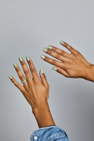 Two hands with mint green manicure and matching ring, one in denim sleeve, posed against a neutral grey backgroundの写真素材