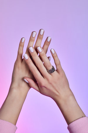 Two hands with soft white manicure and textured silver rings posed against a vibrant pink-purple gradient backgroundの写真素材