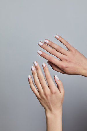 Two hands with soft white manicure gently posed against a neutral grey background, showcasing clean lines and glossy finishの写真素材